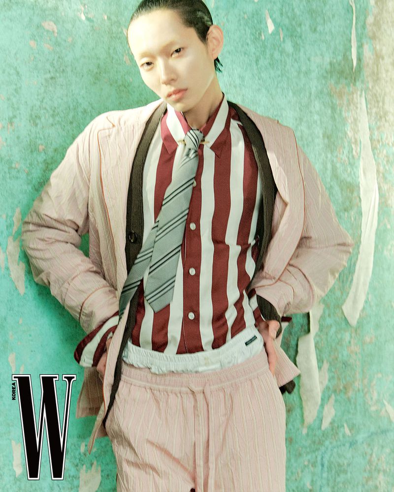Model Minki Kwon in a layered pink suit, striped shirt, and tie against a distressed turquoise wall for W Korea.