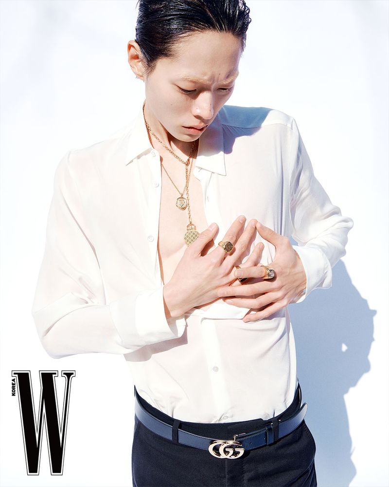 Asian male model wearing an unbuttoned white shirt and gold necklaces against a plain white studio backdrop.