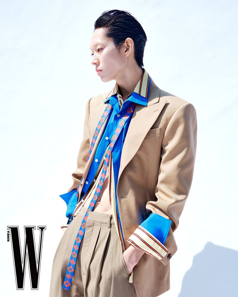 Model Minki Kwon in a layered beige blazer, open blue button-down shirt, and pleated trousers against a white background for W Korea.
