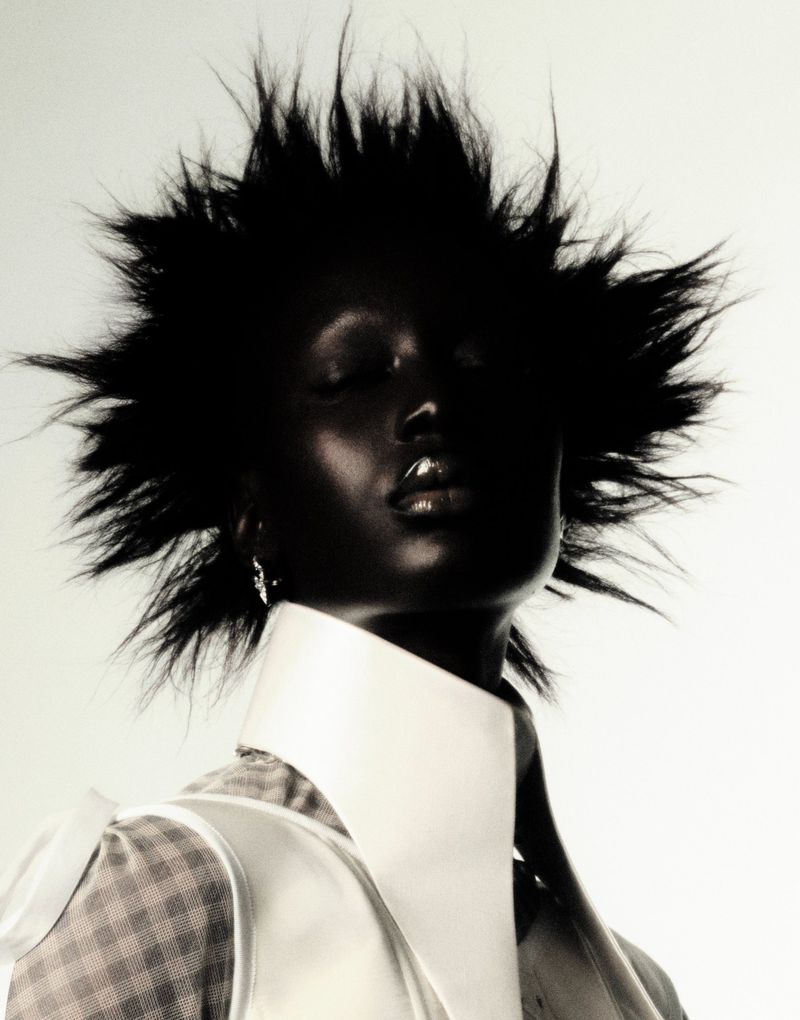 Model Mameanta Wade with spiky black hair wearing an exaggerated high white collar against a bright studio backdrop.