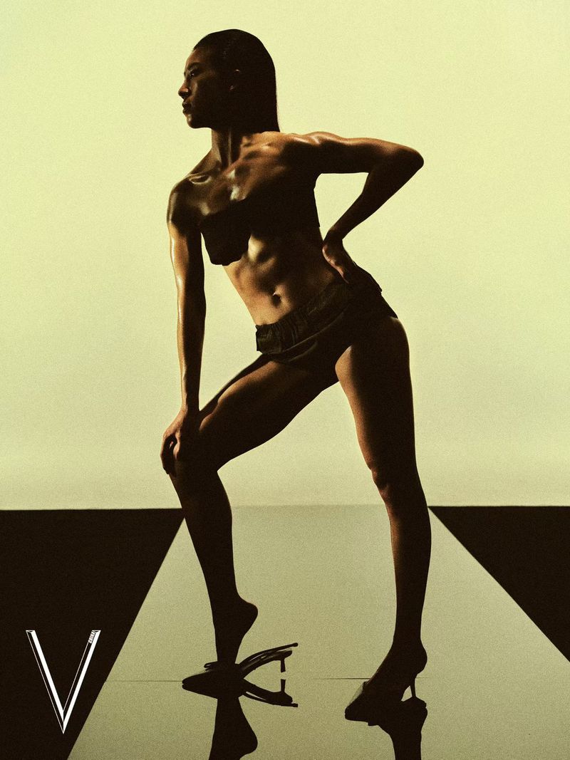 Athletic model posing in black swimwear and heels on a reflective surface for V Magazine China.