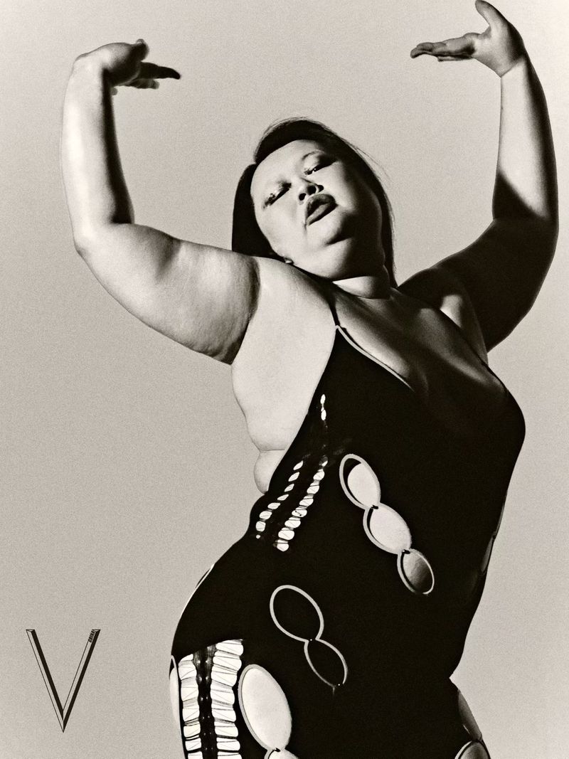 Model in a patterned black dress with arms raised in a dynamic pose against a neutral studio background