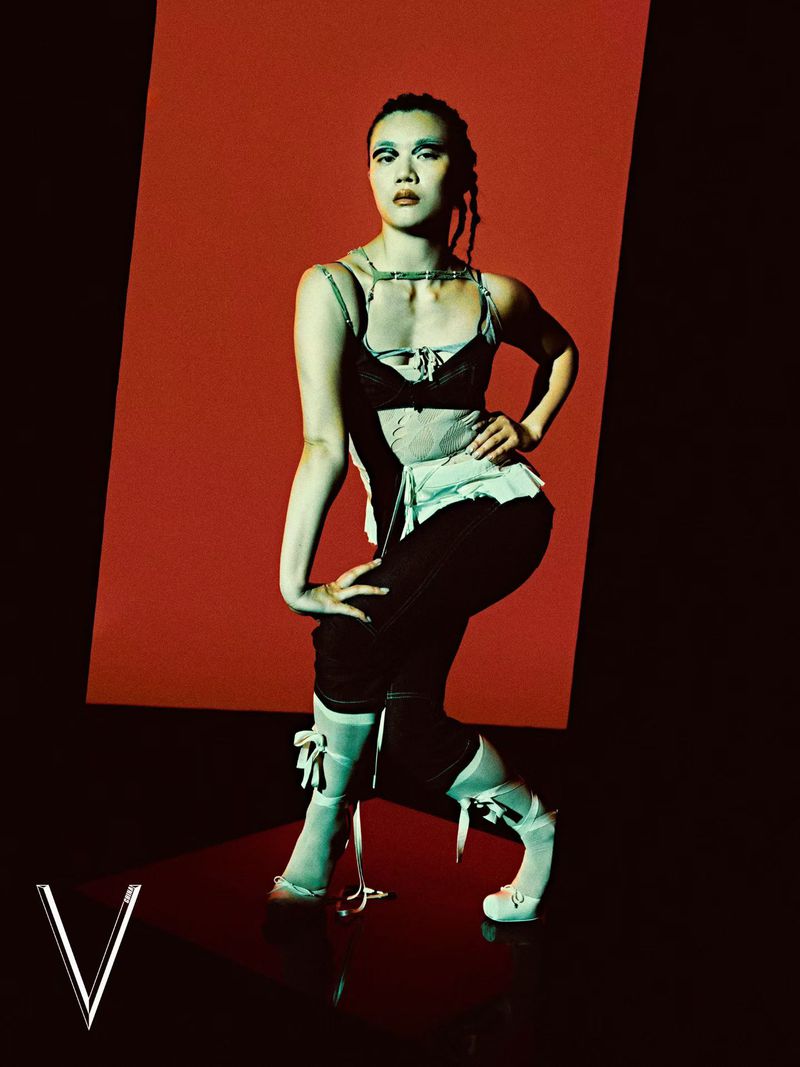 Model posing in a layered black and white corset top with ribbon heels against a graphic red and black background.