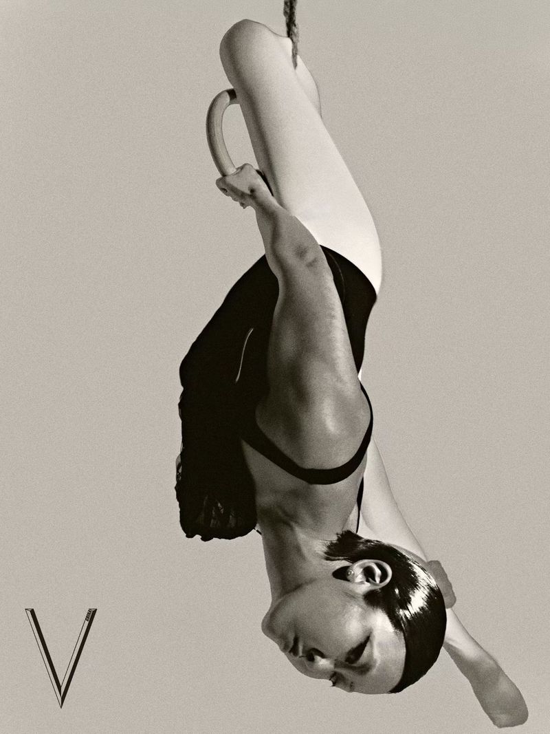 Monochrome image of a person suspended upside down from gymnastic rings, showcasing strength and control against a neutral background.