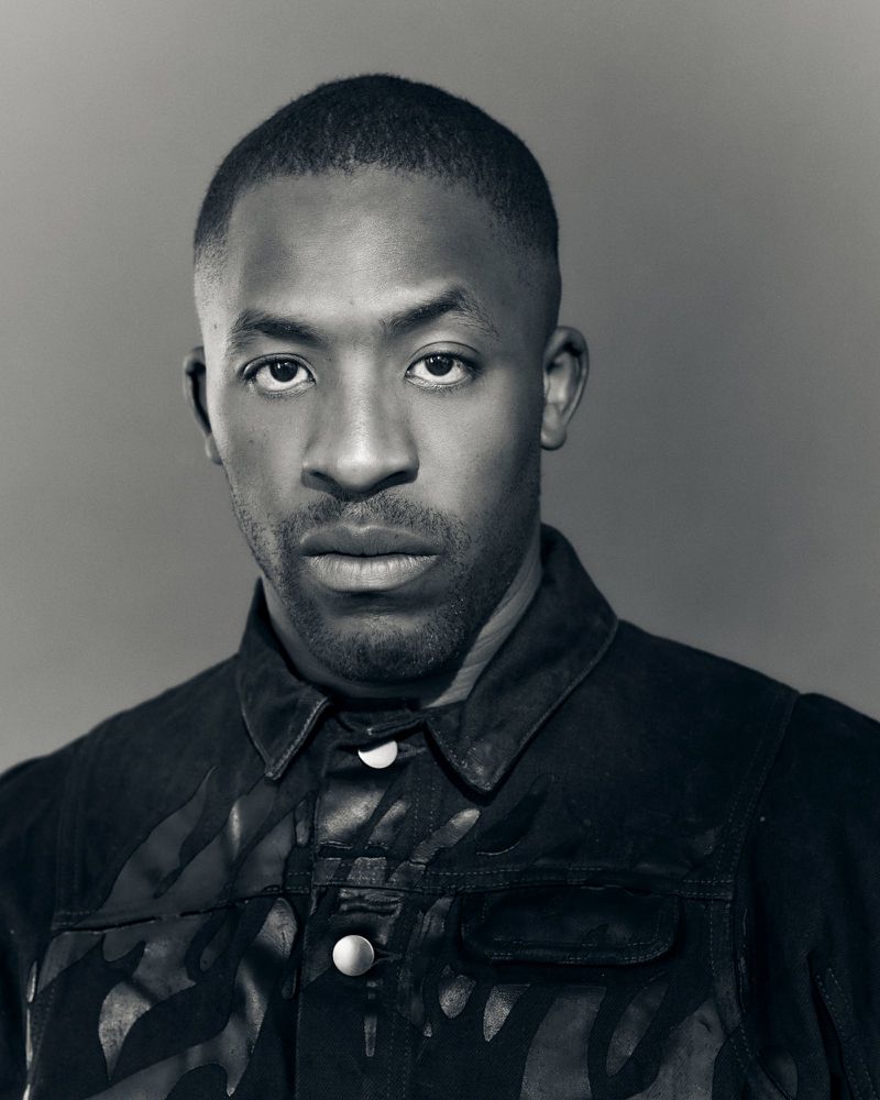 Portrait of an African-American adult male in a patterned jacket against a gray background, showcasing fashion and portrait photography.