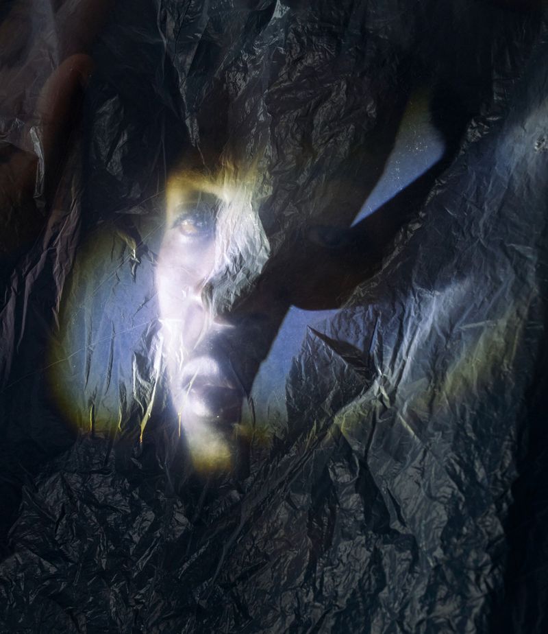 Portrait of James Massiah illuminated with focused dramatic light and viewed through crinkled dark plastic texture.