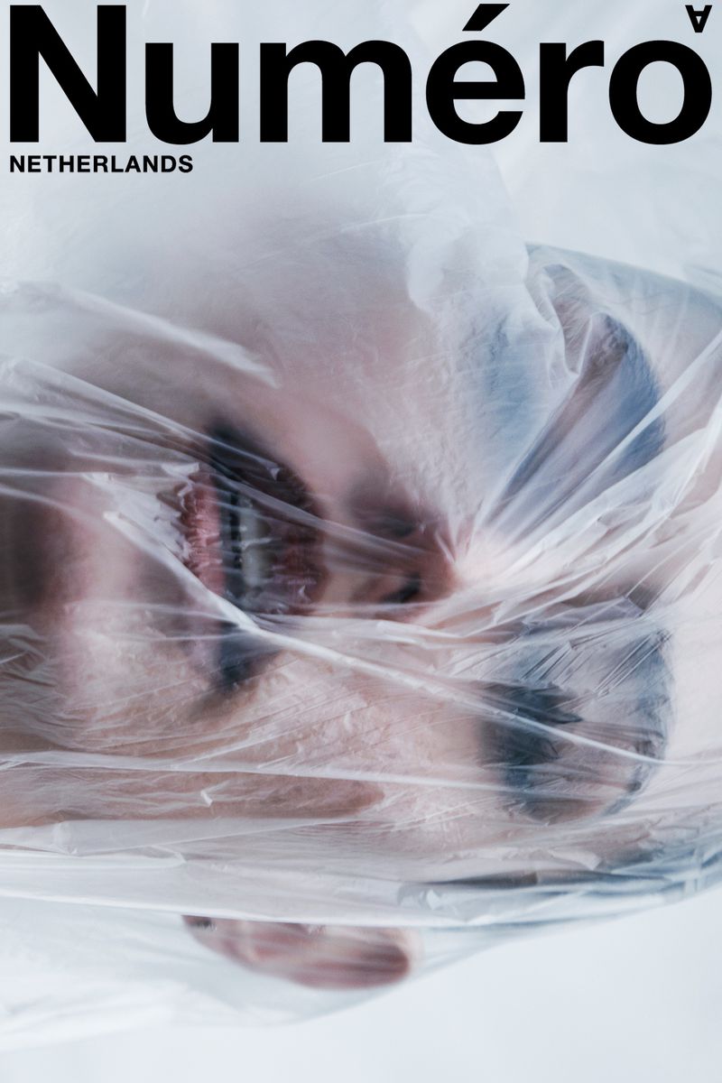 Close-up of a model's face partially visible beneath a sheet of crinkled transparent plastic with Numéro Netherlands typography.