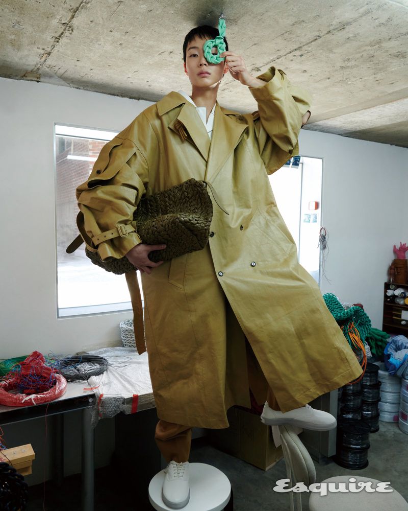Model in oversized beige trench coat holding woven green bag, photographed for Esquire Korea editorial by Pakbae.