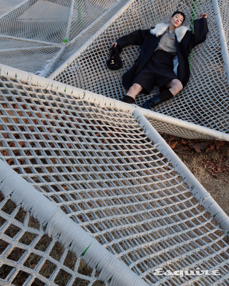 Model Minki Kwon lying on a geometric white rope net wearing a black coat with a fur collar for Esquire Korea.
