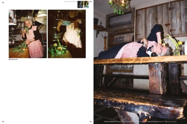 Magazine editorial spread showing artist Michel Auder wearing a pink patterned apron while lying across a rustic wooden table.
