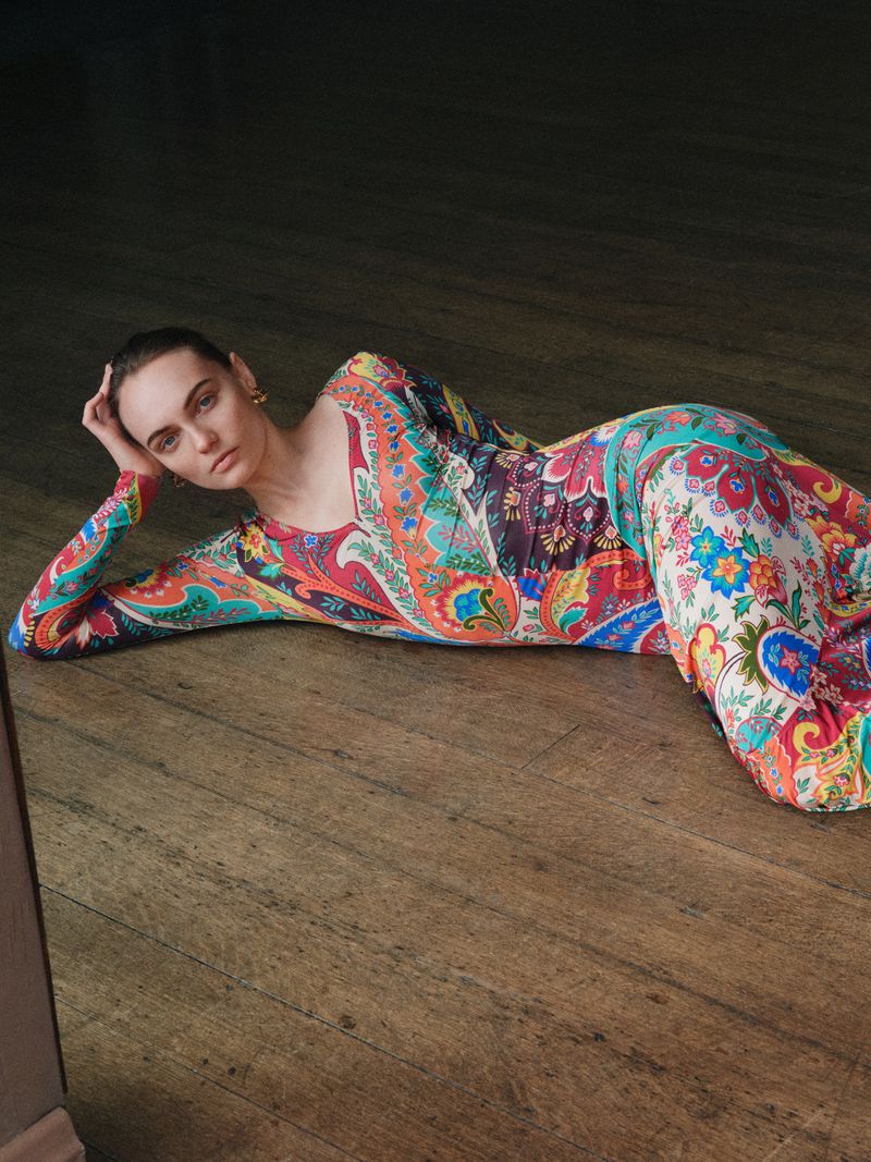 Model Fran Summers reclining on rustic wooden floorboards wearing a vibrant colorful paisley print dress.