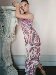 Model leaning against an ornate carved stone pedestal wearing a colourful patterned slip dress