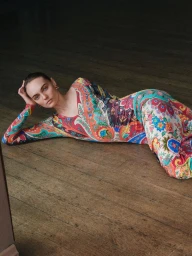 Model Fran Summers reclining on rustic wooden floorboards wearing a vibrant colorful paisley print dress.