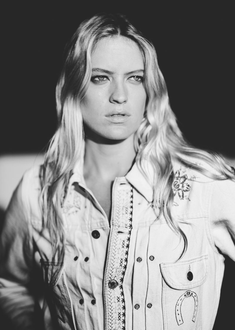 Black and white portrait of model Kat Carter wearing an embroidered western denim jacket against a dark background.