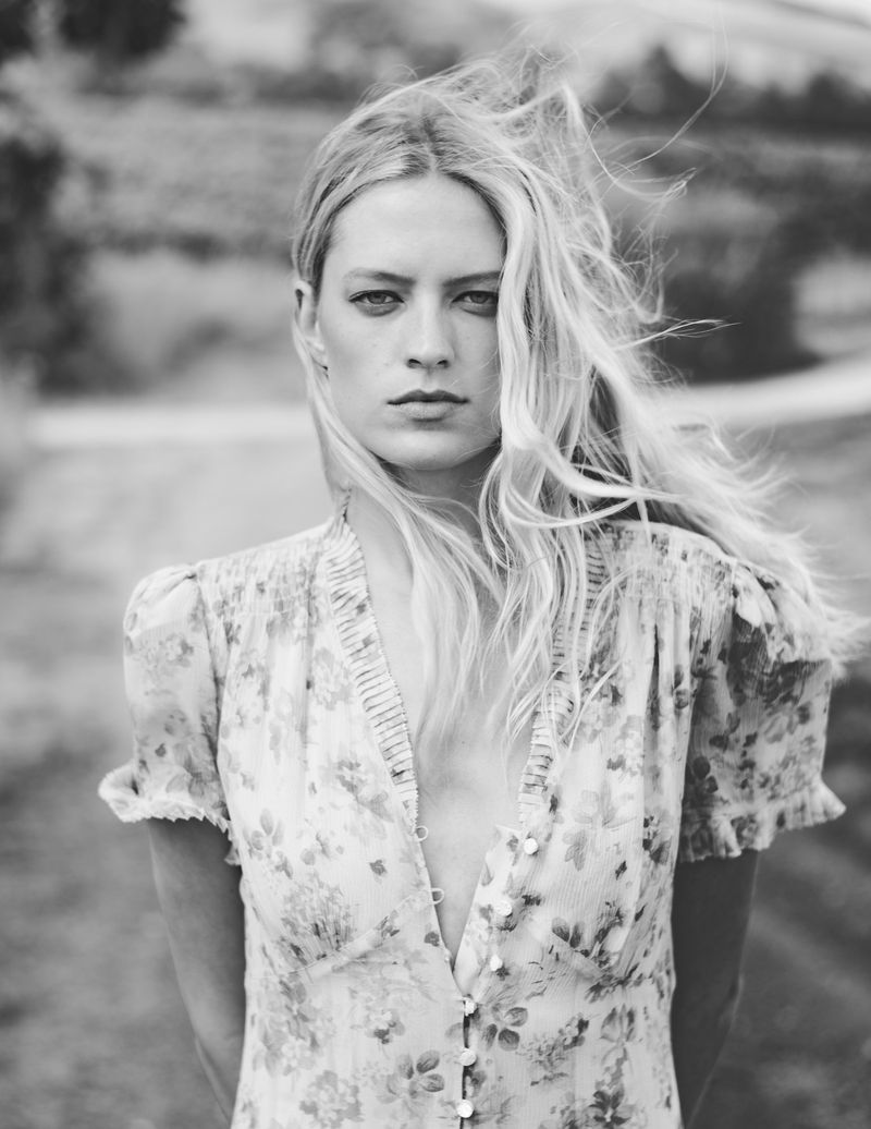 Black and white portrait of model Kat Carter in a ruffled floral dress outdoors with windblown blonde hair.