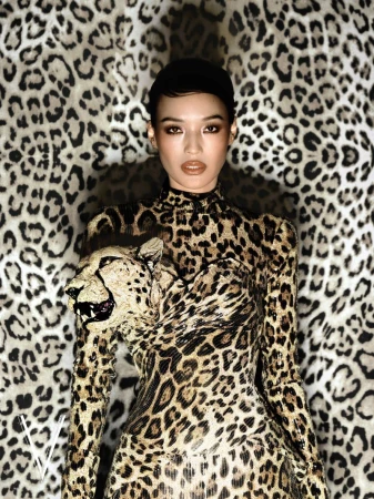 Model wearing a high-neck leopard print dress with a sculptural feline head against a matching animal print backdrop.