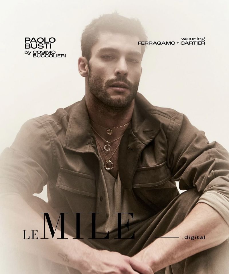 Portrait of a dark-haired male model wearing a brown jacket and layered pendant necklaces for a jewelry and fashion advertisement.