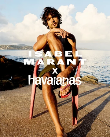 Model Marlon Teixeira seated on a red plastic chair by the coast for the Isabel Marant x Havaianas campaign.