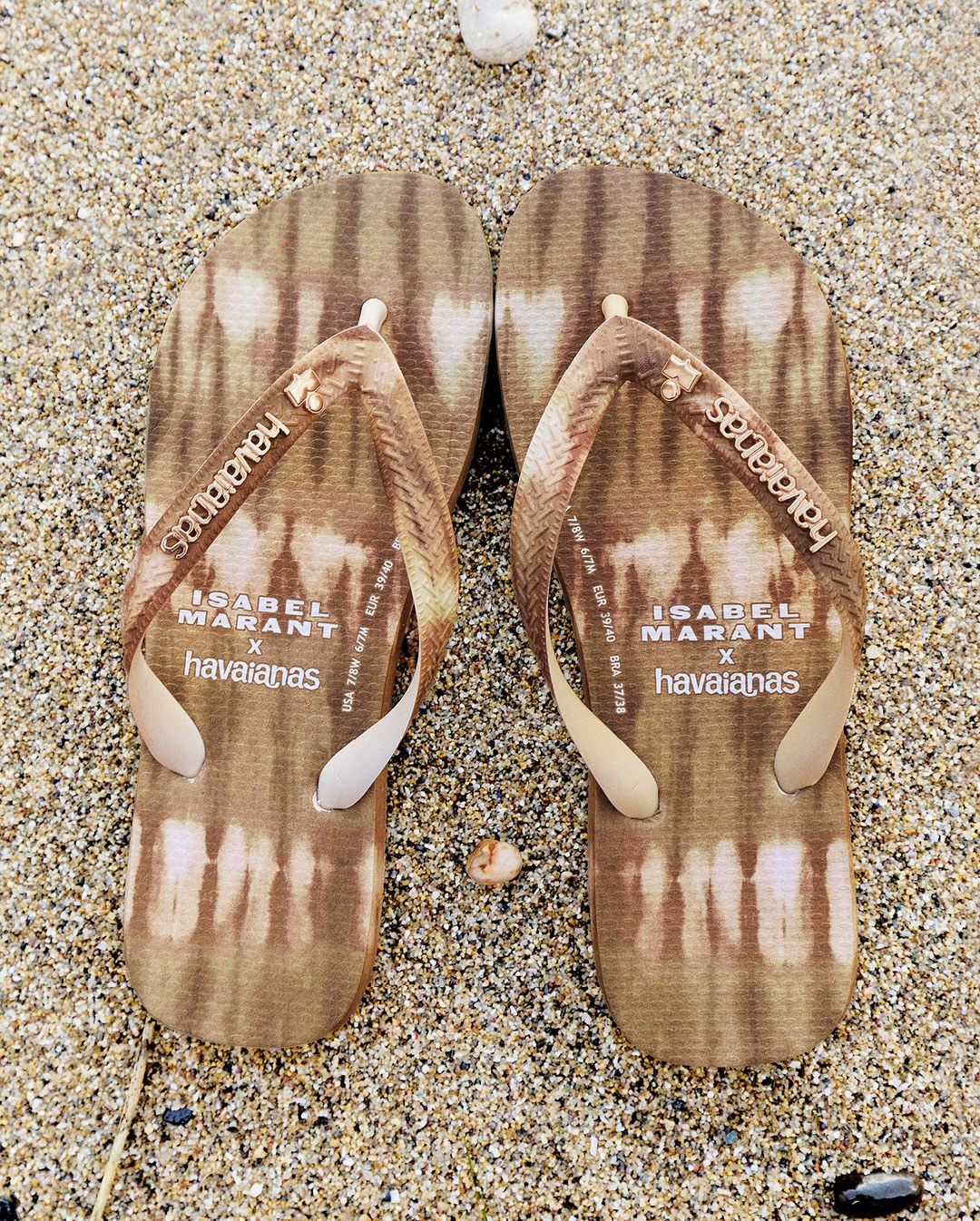 A pair of Isabel Marant x Havaianas printed flip-flops resting on coarse beach sand.