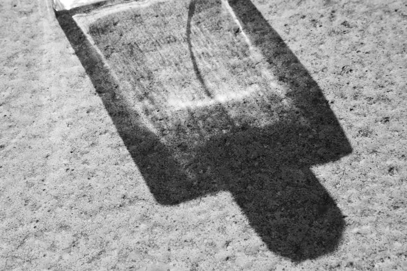 Monochrome photograph capturing the hard shadow and light refraction of a perfume bottle on a textured stone surface.