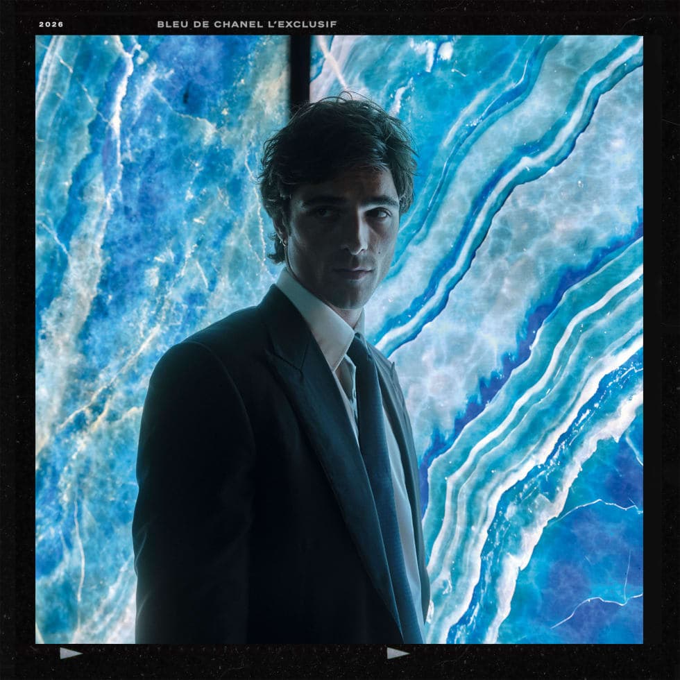 Jacob Elordi wearing a dark tailored suit and tie against a glowing blue marbled background for Bleu De Chanel.