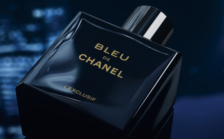 Bleu de Chanel L'Exclusif perfume bottle in dark navy glass with gold lettering tilted in dramatic low lighting.