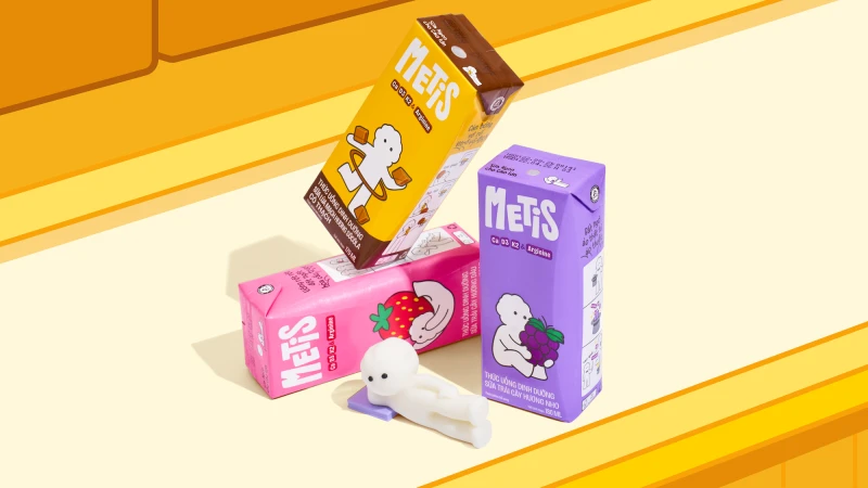Three colorful METIS drink cartons in yellow, pink, and purple arranged with a white clay figurine on a warm yellow surface.