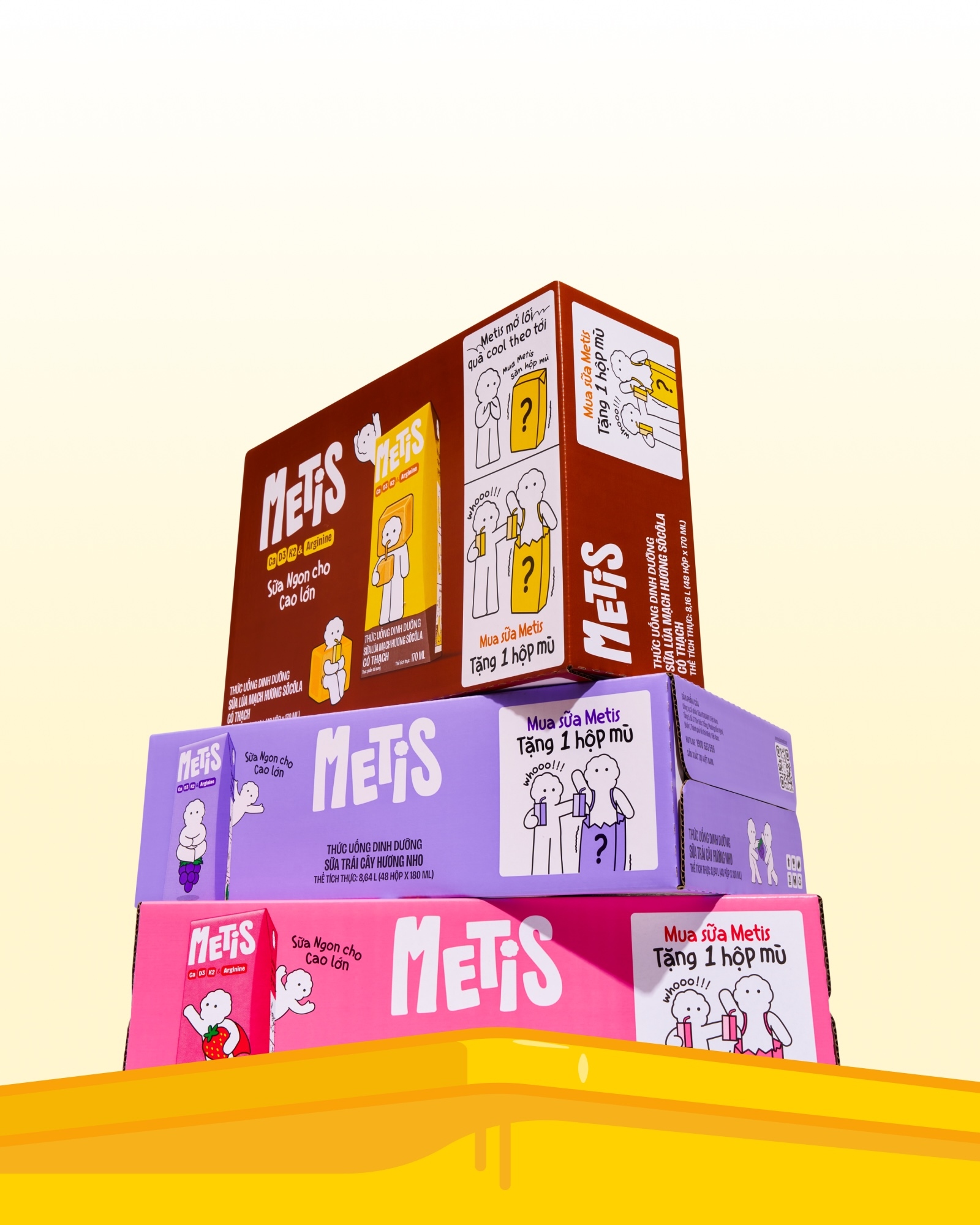 Stack of three colorful METIS drink packaging boxes in pink, purple, and brown resting on a yellow surface against a pale background.