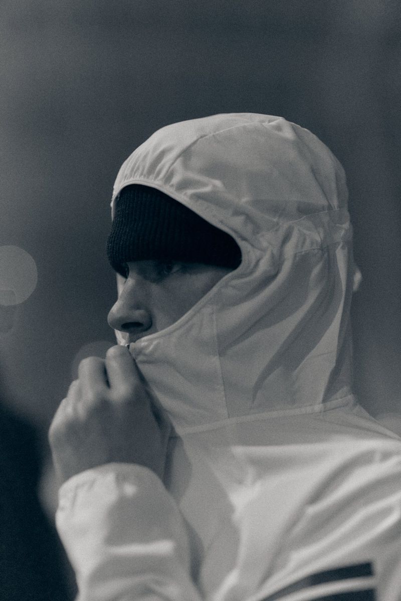 Side profile of a person wearing a black beanie and white hooded jacket zipped high over their lower face.