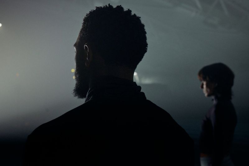 Silhouette of a man facing away in a misty dark setting with a woman standing in profile in the background.