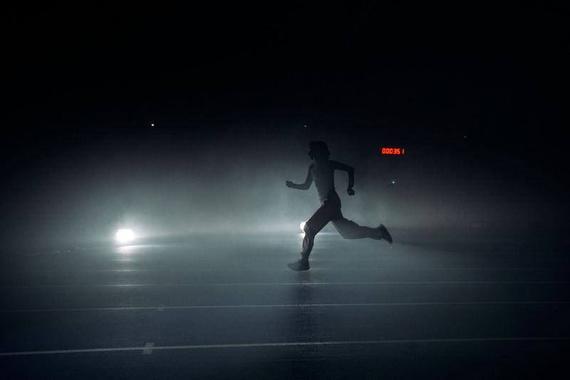 Silhouette of a runner in mid-stride across a dark, misty athletic track with backlighting and a glowing red timer.