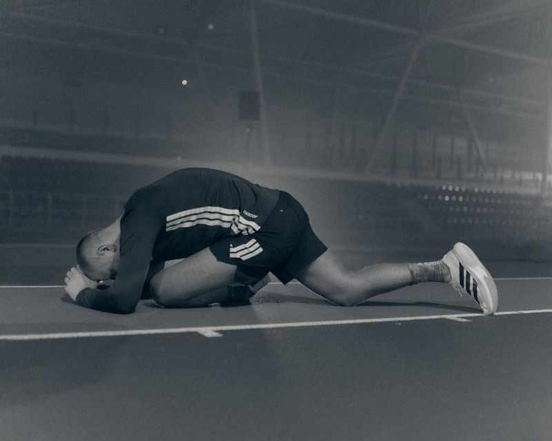 Runner in black Adidas athletic wear lying face down on a track in a foggy stadium.