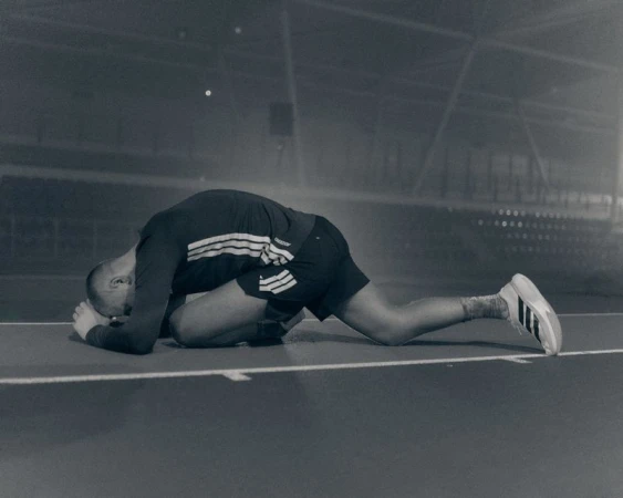 Runner in black Adidas athletic wear lying face down on a track in a foggy stadium.