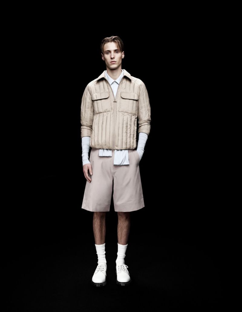 Model Robin Avignon poses against a black background wearing a beige quilted jacket, matching tailored shorts, and white shoes.