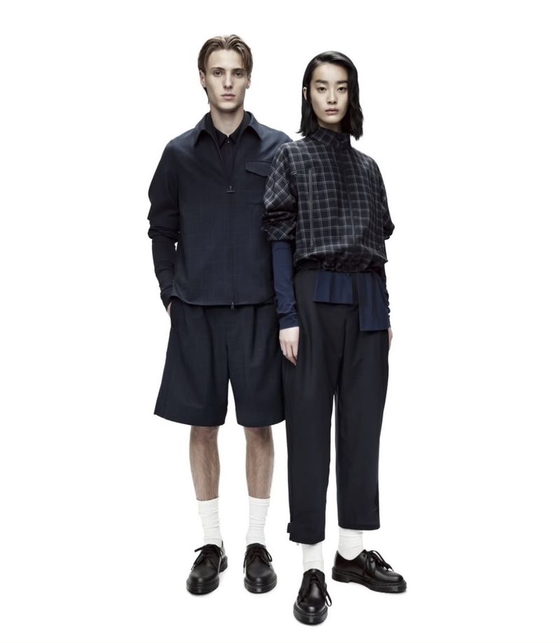 Two fashion models in dark navy and black casual outfits pose in a photo studio with a bright white backdrop and soft lighting.