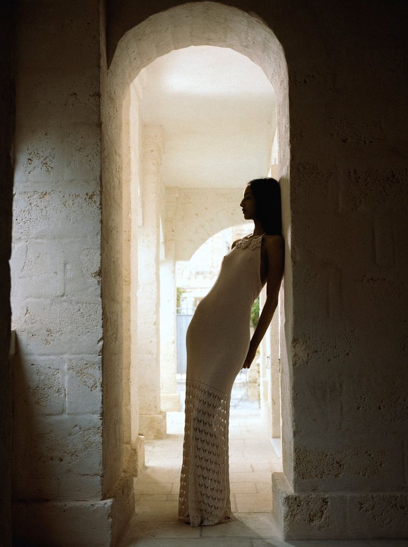 Model Mona Tougaard leans against a stone archway in a long knit dress in a Vogue Italia fashion editorial.