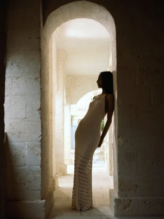 Model Mona Tougaard leans against a stone archway in a long knit dress in a Vogue Italia fashion editorial.