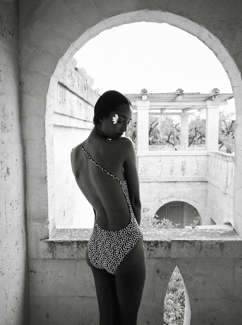 Black and white photo of Mona Tougaard seen from behind in a backless patterned swimsuit, framed by a stone arch.