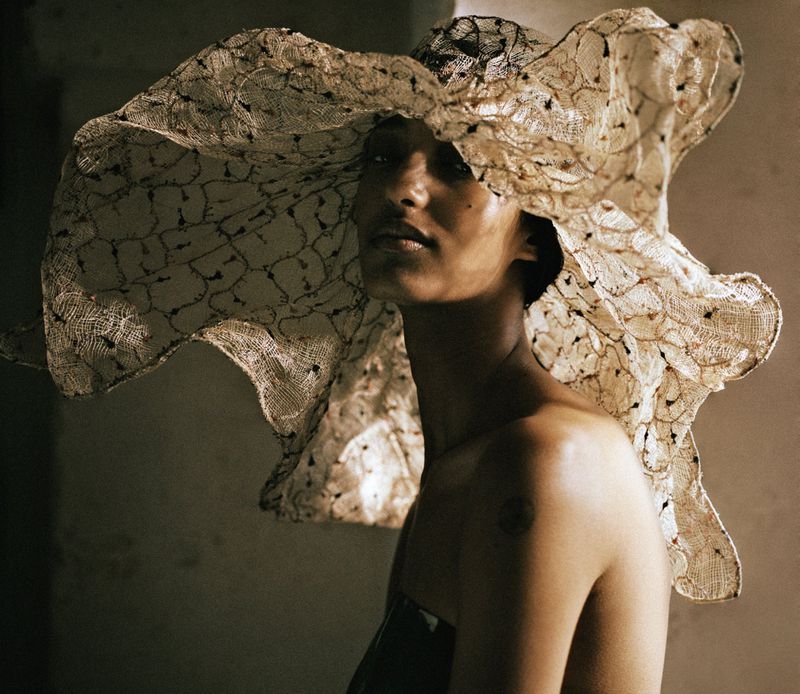 Mona Tougaard wearing an exaggerated wide-brim sheer lace hat and strapless bodice in soft directional lighting.