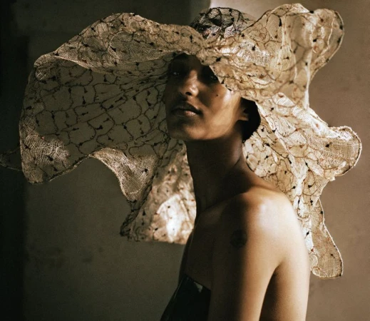 Mona Tougaard wearing an exaggerated wide-brim sheer lace hat and strapless bodice in soft directional lighting.