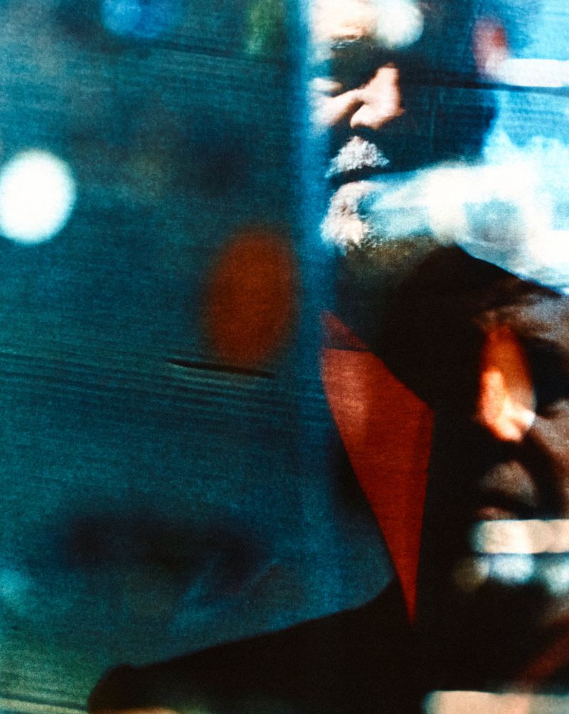 Abstract layered portrait of filmmaker Pedro Almodóvar in blue and red tones with blurred light reflections.