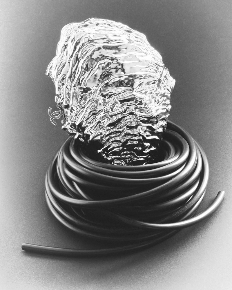 Chrome metallic textured sculpted head form resting inside a coil of black rubber tubing on a dark studio surface.
