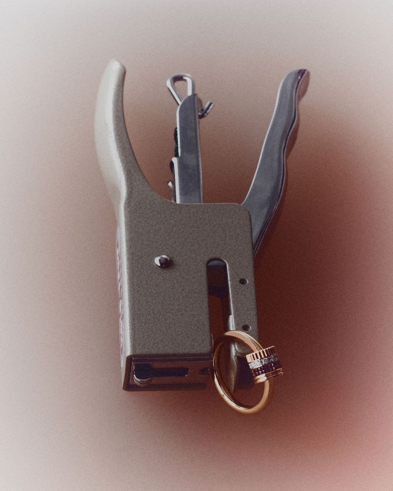 A metal hand stapler holding a luxury gold and diamond ring against a soft muted background.