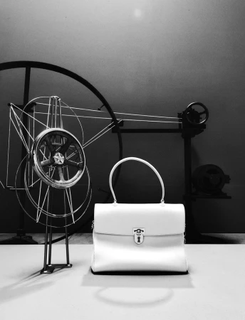 White structured leather handbag with a metallic clasp lock set before mechanical wire wheels in a black and white studio still life.