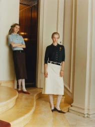Two female models posing on curved stone stairs in an upscale interior for a WSJ fashion editorial shoot.