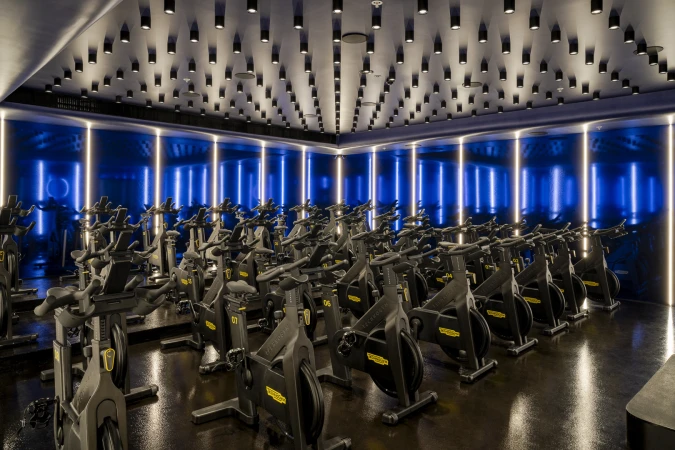 View of exercise bikes in a fitness studio with rows of stationary bikes, shiny black floor, and overhead lights creating a modern gym atmosphere.