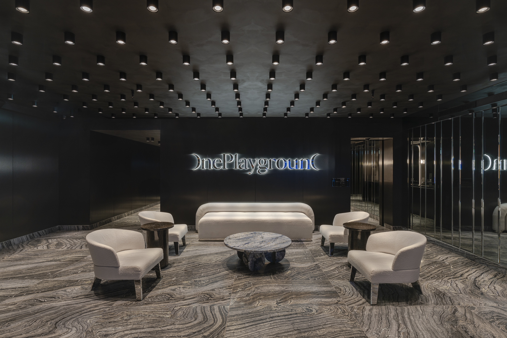 Modern hotel lobby area with seating, marble floors, and recessed lighting in a sleek, minimalist design scheme.