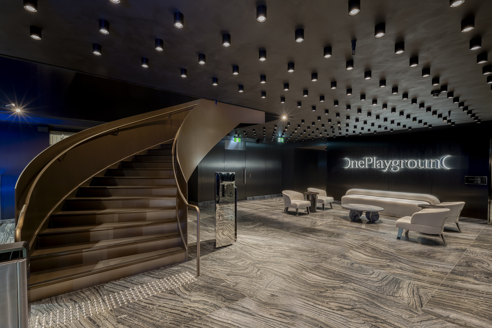 Interior view of a modern lobby with a spiral staircase, textured flooring, recessed lighting, and contemporary furniture in a muted color palette.