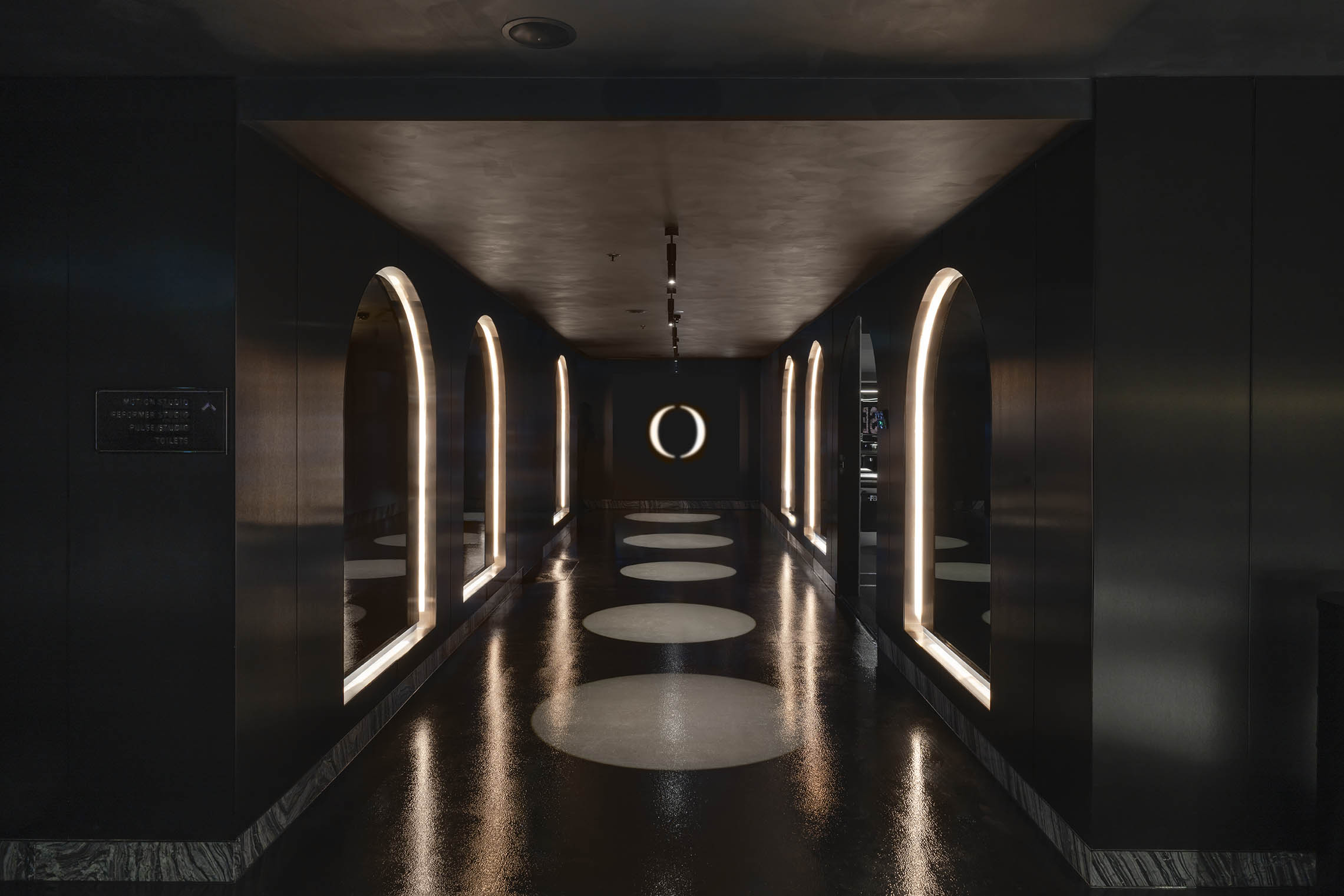 Hallway with a symmetrical design featuring dark walls, a reflective floor, and arched, illuminated doorways. Modern interior design.