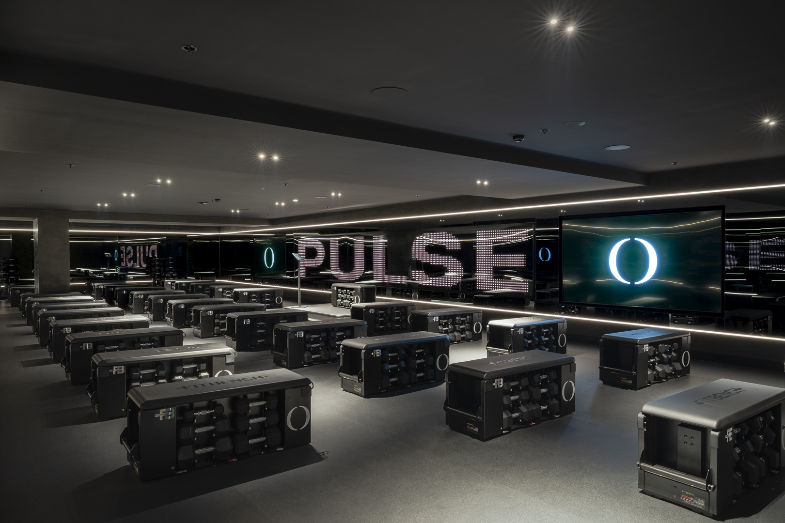 Fitness studio interior featuring rows of workout stations with weights, illuminated 'PULSE' text, and a modern, dark-themed design.